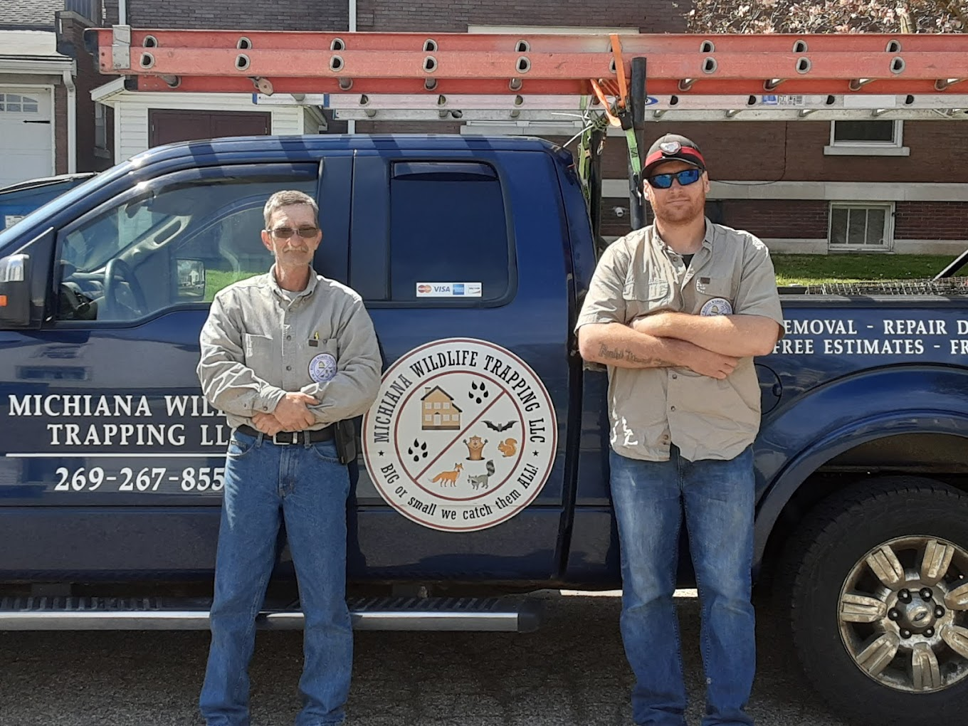 two wildlife removal specialists standing in front of a Michiana Wildlife truck